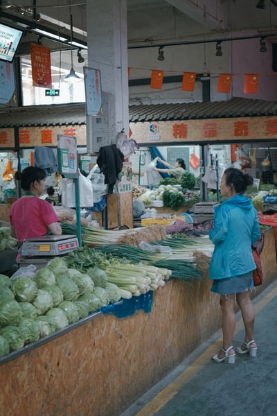 A woman dressed in a red shirt standing in vegetable stall
